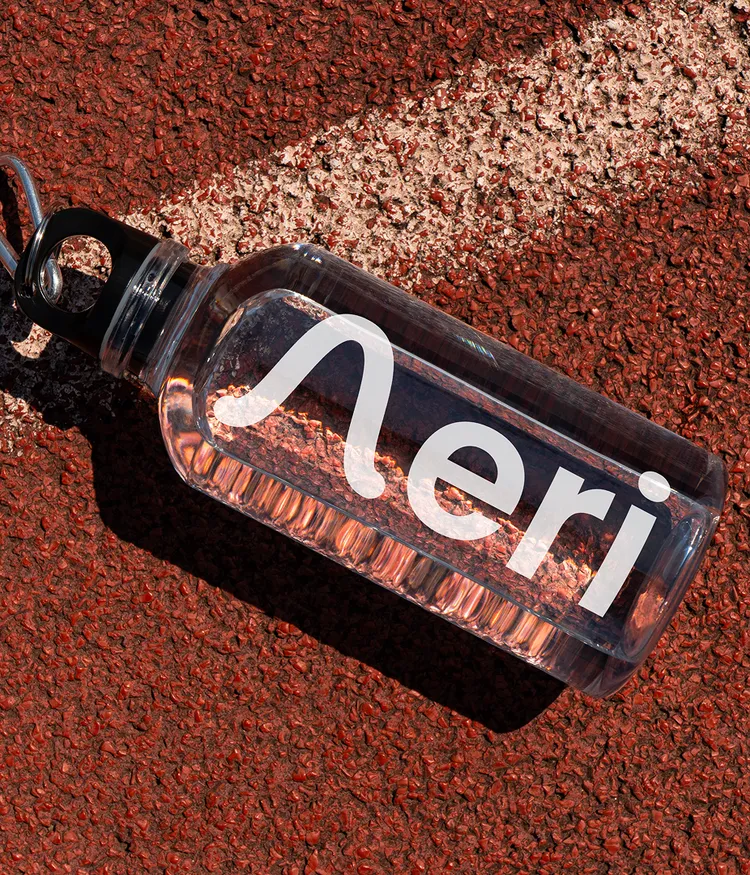 Eine durchsichtige Trinkflasche mit weißem Aeri App Logo, die auf einer Tartanbahn liegt