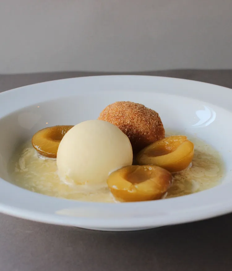 Ein Gericht aus der Küche Maquis mit Krapfen, Eis und flambierten Pflaumen.