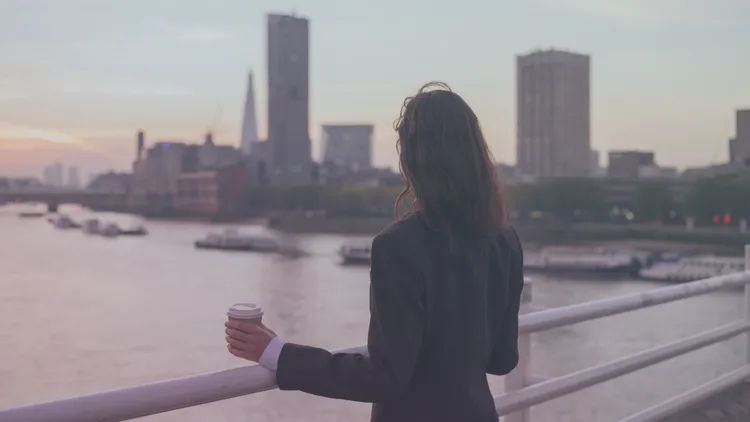 Büroangestellte schaut hoffnungsvoll von einer Brücke auf die Skyline ihrer Stadt
