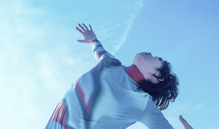 Eine Person tanzt unter einem klaren, blauen Himmel.