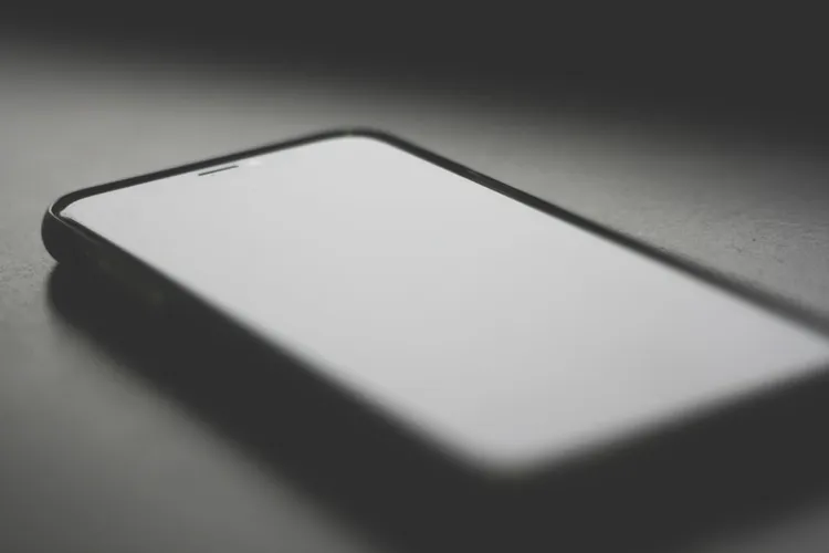 A smartphone is lying face up on a dark surface. The focus is on the upper left corner of the device.